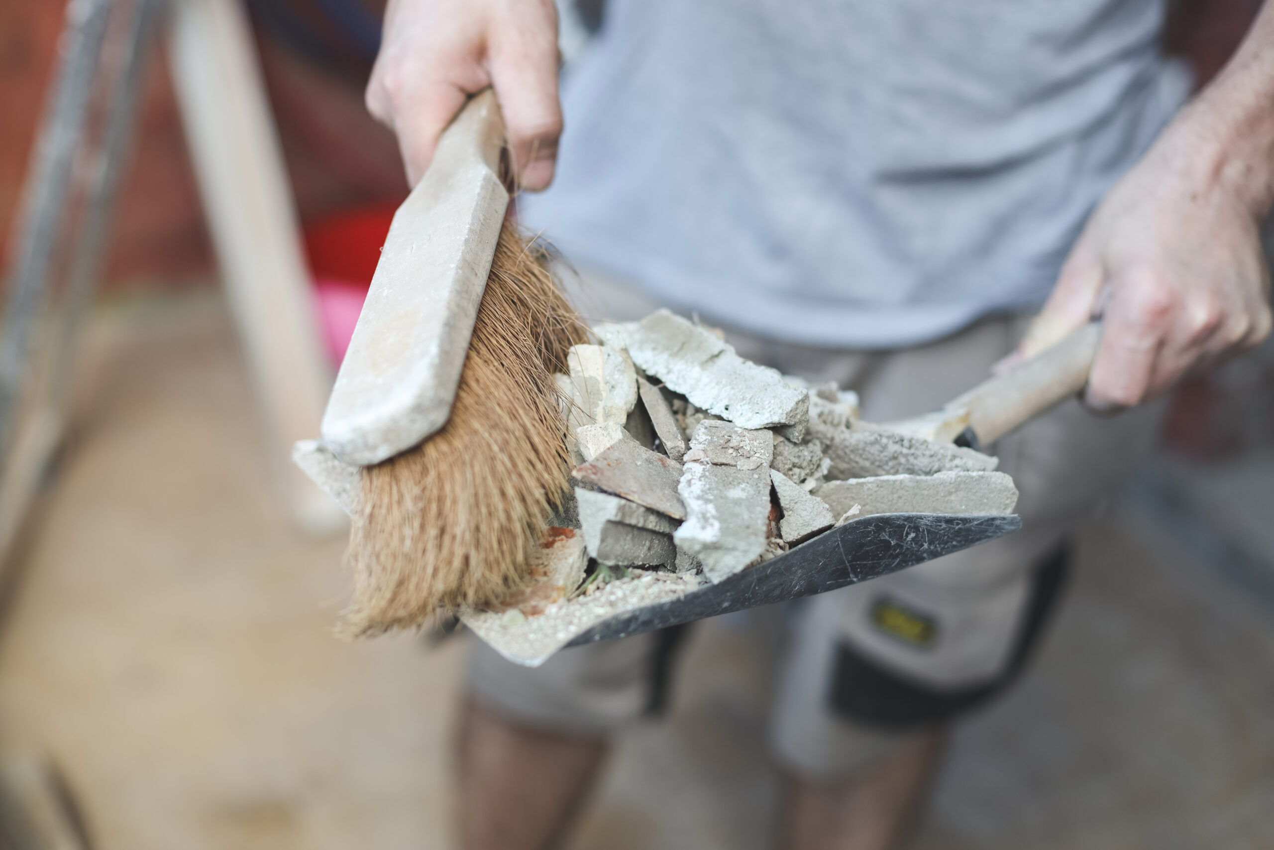 A young Caucasian man holds a scoop with construction waste and a broom to throw it into a bag